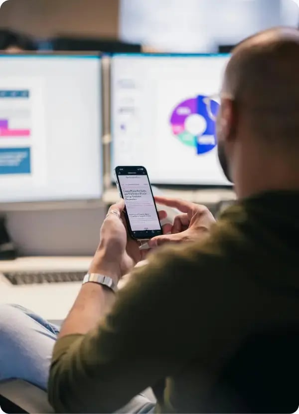 Man checking his phone in front of screens showing business reports Man checking his phone in front of screens showing business reports